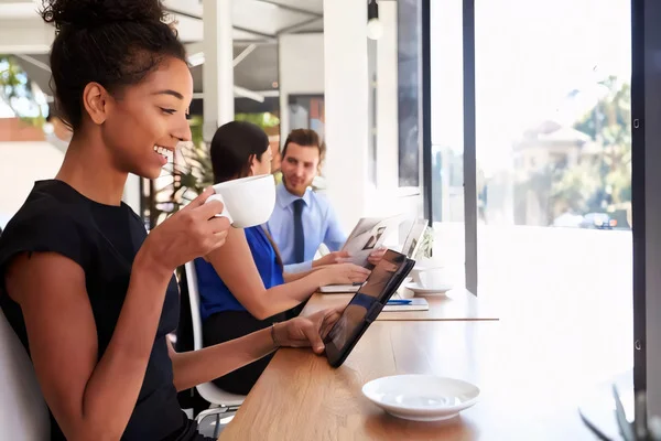 Relaxed lifestyle at Ritiro Apartments: woman drinking coffee and browsing on tablet in a coffee shop setting near Peccole Ranch Las Vegas